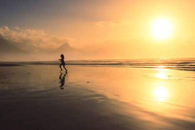Scenic view of beach on a misty day at sunset, silhouette of little girl running with reflection 