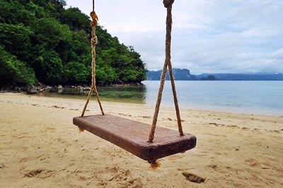 Empty swing on beach against sky