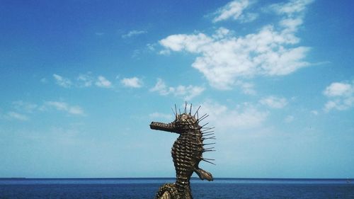 Animal sculpture by sea against sky