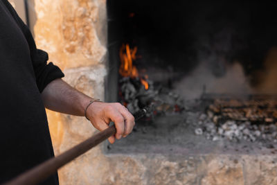 Unrecognizable man is holding a toal for the charcoals in the barbecue while food is being cooked.