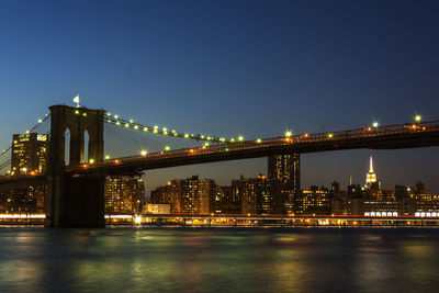 Illuminated brooklyn bridge over east river against sky