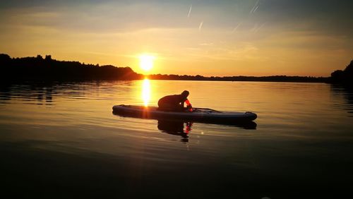 Man in boat on lake against sky during sunset