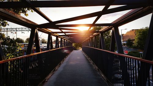 Footbridge amidst trees against sky during sunset