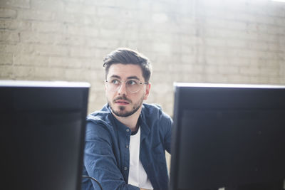 Young entrepreneur looking away while working on computer programs in creative office