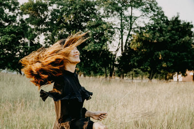 Smiling young woman tossing hair while standing on field