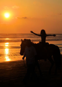 Silhouette people with horse at beach against sky during sunset
