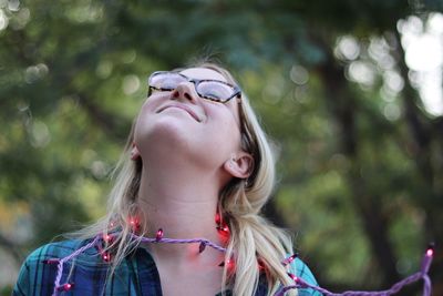 A young woman smiles as she stands outside in purple lights, with trees in the background.