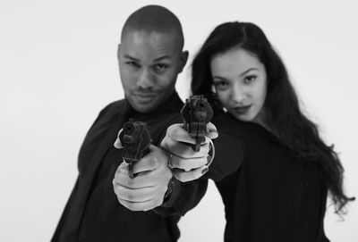 Portrait of fashionable gangster friends aiming gun at camera against white background