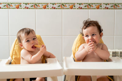 Funny babies sitting in dining chair and eating bread