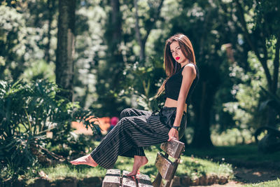Woman sitting on tree trunk amidst plants in forest