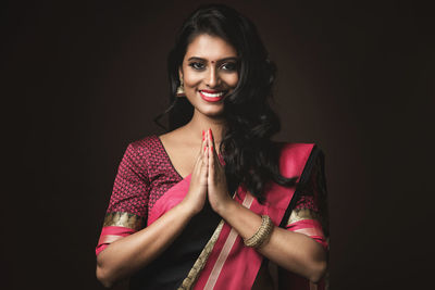 Portrait of young woman standing against black background