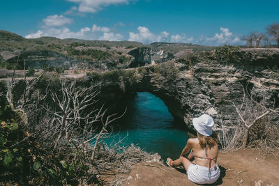 Rear view of woman sitting against sea and landscape