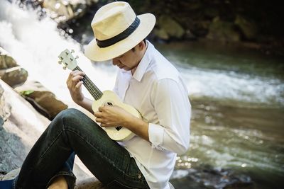 Man playing ukulele while sitting by river