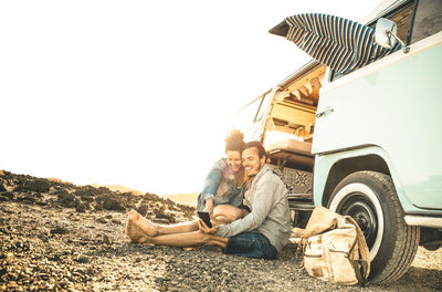 Couple sitting by van against sky