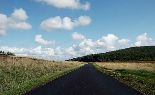 Empty road amidst field against sky