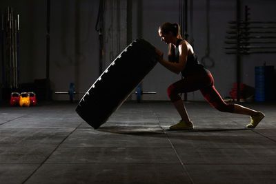 Side view of woman pushing tire at gym