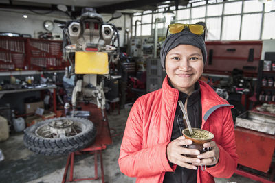 Portrait of woman drinking mate tea in motorbike mechanics workshop