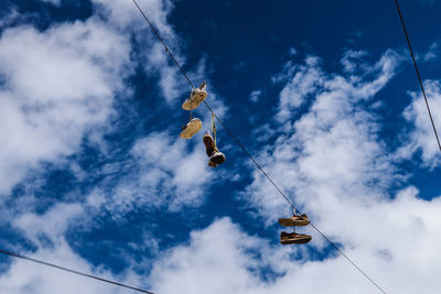 Low angle view of shoes hanging on rope against sky