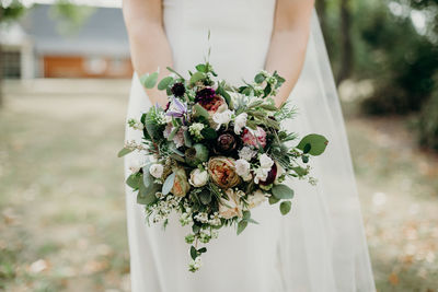 Midsection of bride holding bouquet while standing outdoors