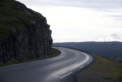 Empty road leading towards mountain against sky