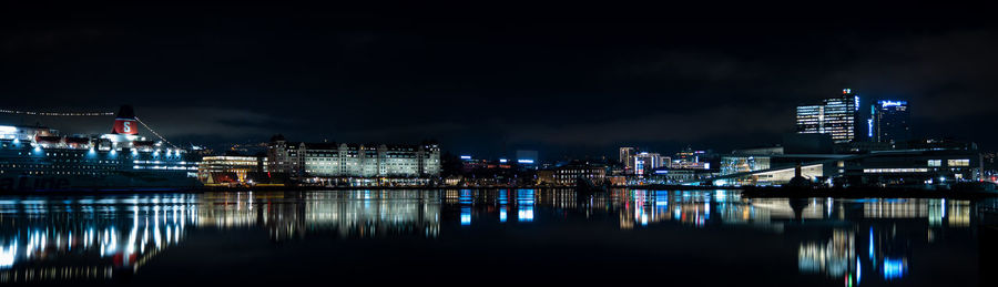 Illuminated buildings by river against sky at night