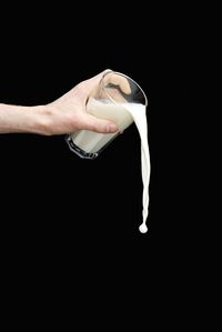 Cropped hand spilling milk against black background