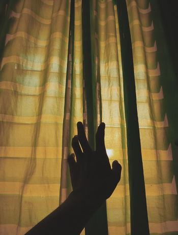 Cropped hand touching curtain at home
