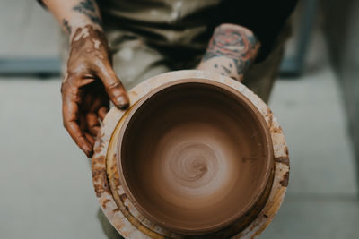 Closeup of dirty hands of anonymous craftsman using pottery wheel and making clay pot in workshop