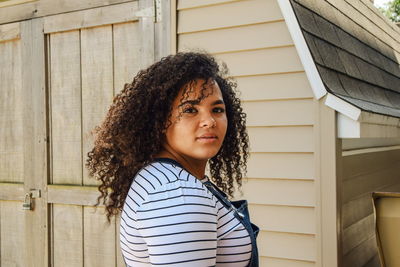 Portrait of young woman standing against log cabin 