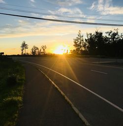 Road by trees against sky during sunset