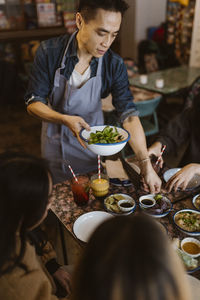 Waiter serving serving food and dumplings to customers at restaurant