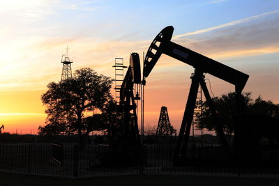 Pump jacks and drilling rig at sunset, oilfield silhouette