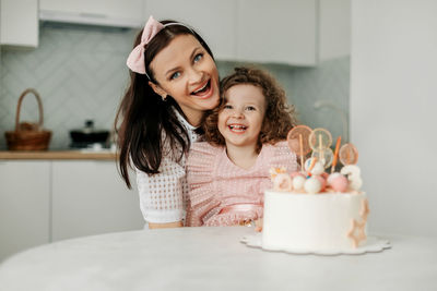 Portrait of a laughing mother and daughter with a birthday cake in the kitchen. birthday, holiday.