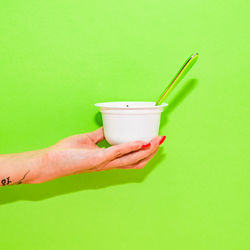 Cropped image of hand holding drink against green background