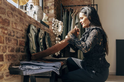 Female owner folding clothes while sitting at boutique