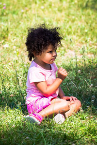 Mixed race girl with dark brown curly hair and pink clothes putting a piece of grass in her mouth