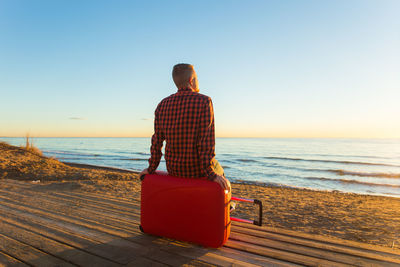 Rear view of man looking at sea against sky during sunset