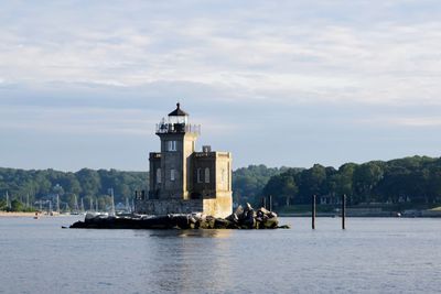 Lighthouse amidst sea and buildings against sky