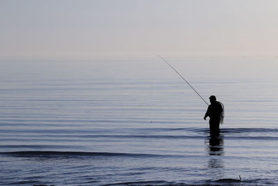 Man fishing in sea against sky