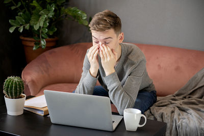 Young frustrated man sitting on sofa at home