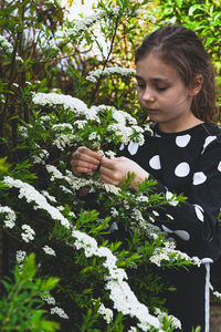 Cute girl holding flowering plant while standing outdoors