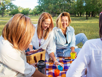 Women on a picnic pouring coffee from a thermos sitting on a picnic blanket,trip to nature,