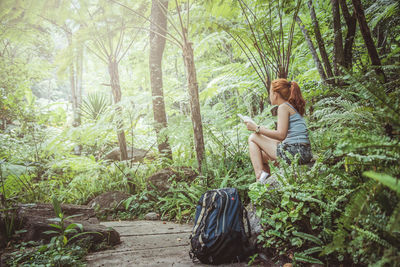 Side view of young woman with book sitting in forest