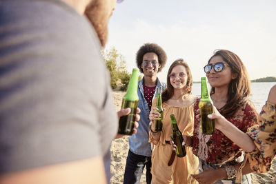 Happy friends with beer bottles standing at beach