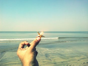 Close-up of hand holding sand at beach against clear sky