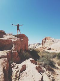 Low angle view of woman standing on rock against clear sky