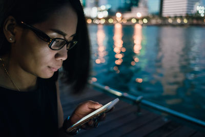 Close-up of young woman using mobile phone by river at night