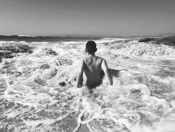 Rear view of shirtless man looking at sea against sky