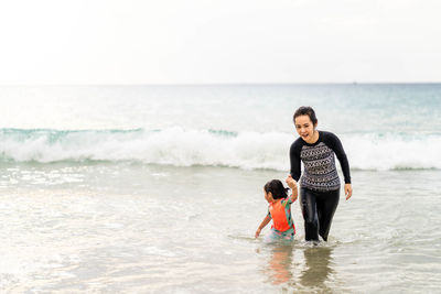 Full length of mother and daughter on beach against sky