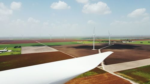 Cropped image of windmill turbine by agricultural landscape against sky